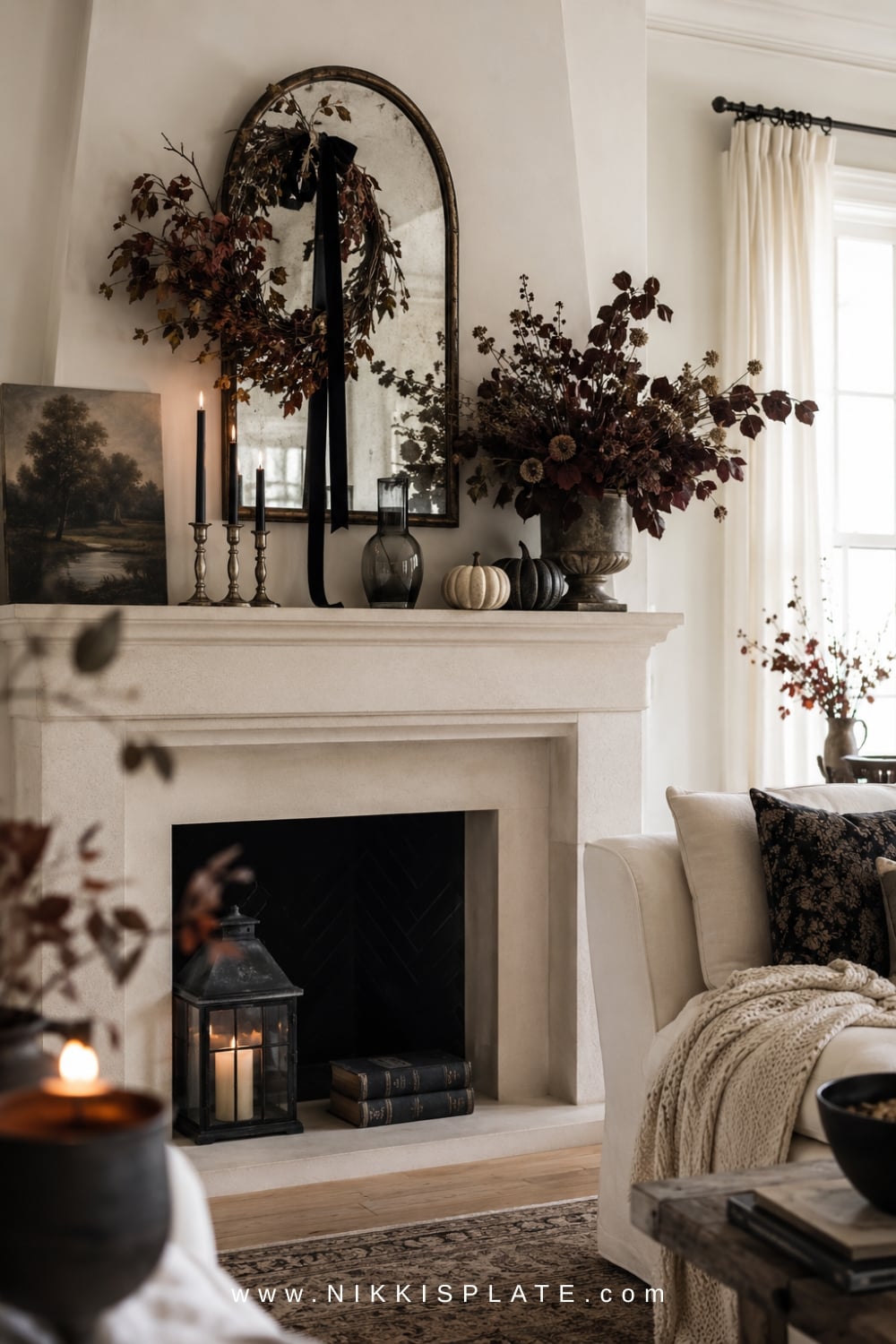 Elegant Halloween mantel with black candles, vintage artwork, leafy garland, and neutral pumpkins