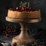 Side view of cherry cheesecake on a wooden cake stand, topped with fresh whole cherries and rustic table decor.