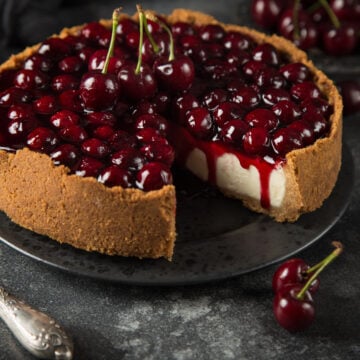 Cherry cheesecake with a slice removed, showing creamy filling and cherry topping dripping onto the graham cracker crust.