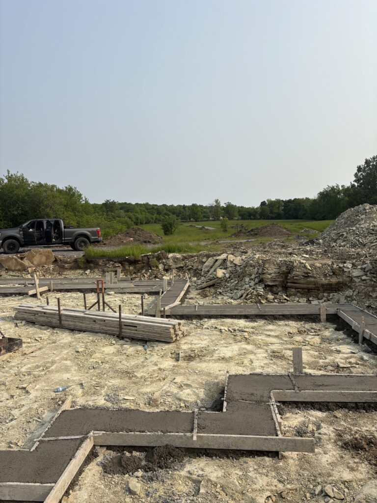 Concrete footings set in rocky excavation area, with piles of earth and gravel in the background.