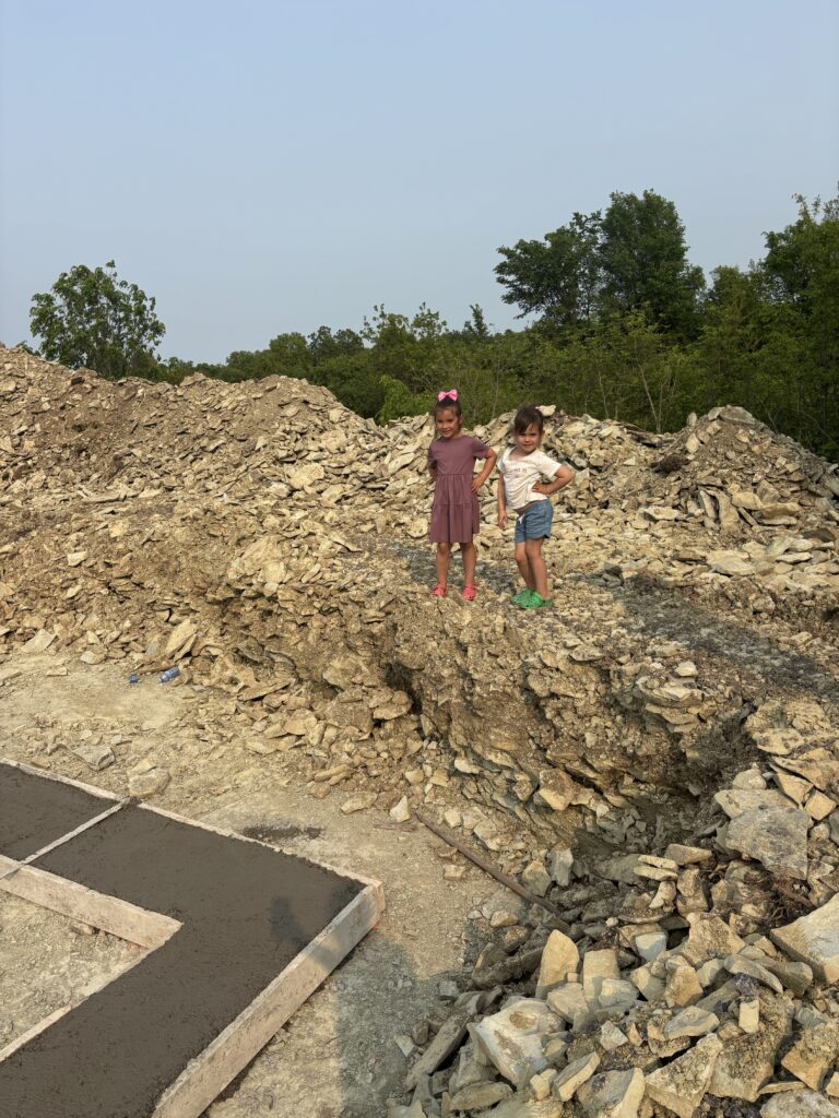 Two young children standing proudly on a pile of excavated rock during the home build process.