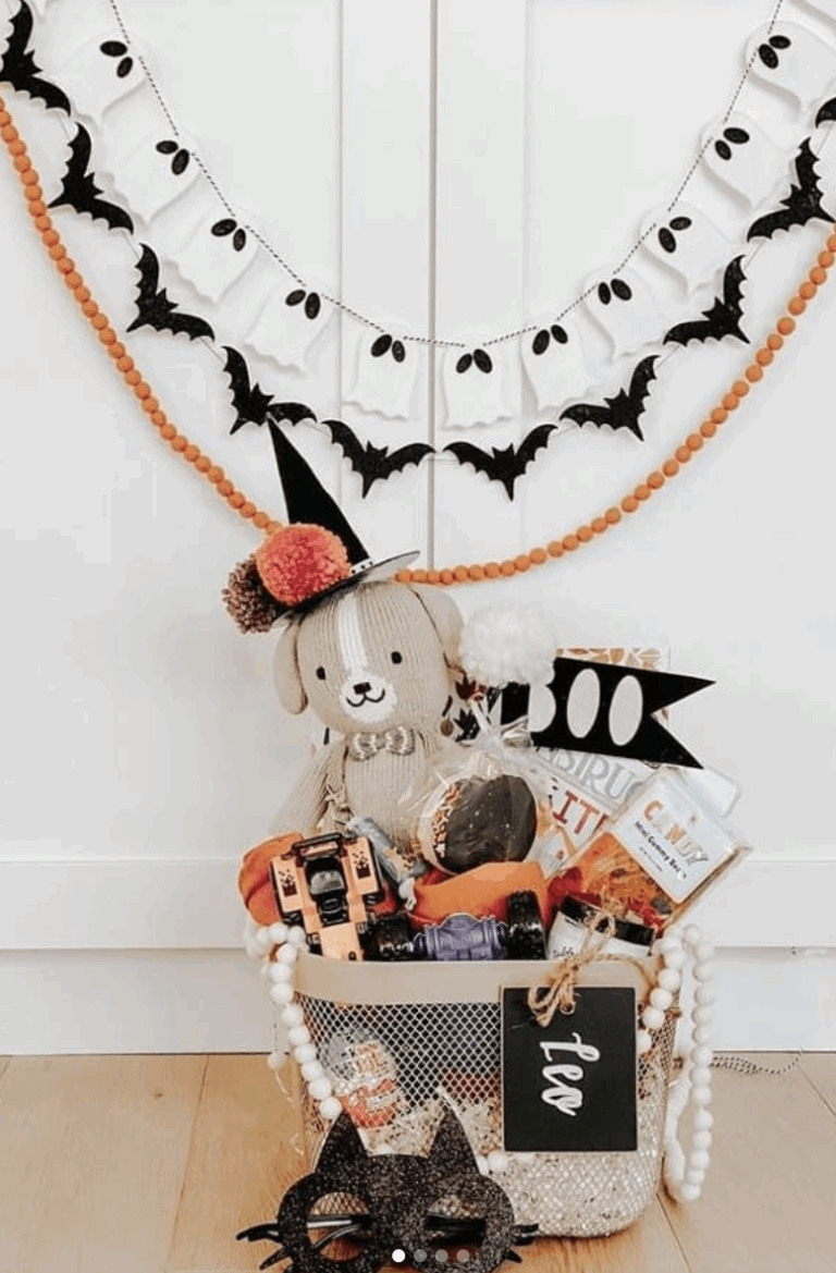 Neutral Halloween boo basket with a plush dog toy, festive treats, and black cat mask, displayed under ghost and bat garland decor