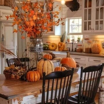 Rustic farmhouse kitchen with pumpkins, fall foliage, and vintage decor on a distressed wood table under warm lighting.