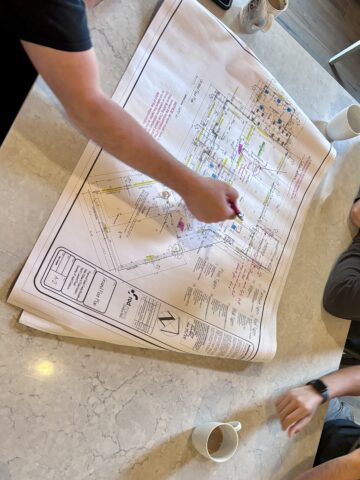 People reviewing and marking up custom farmhouse blueprints on a kitchen counter during a home design meeting
