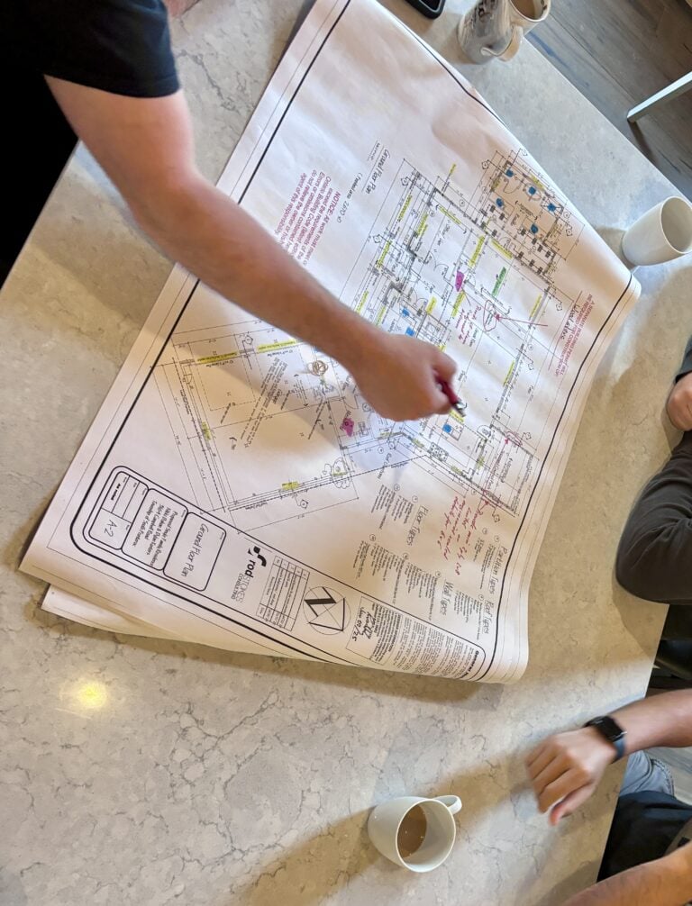 People reviewing and marking up custom farmhouse blueprints on a kitchen counter during a home design meeting