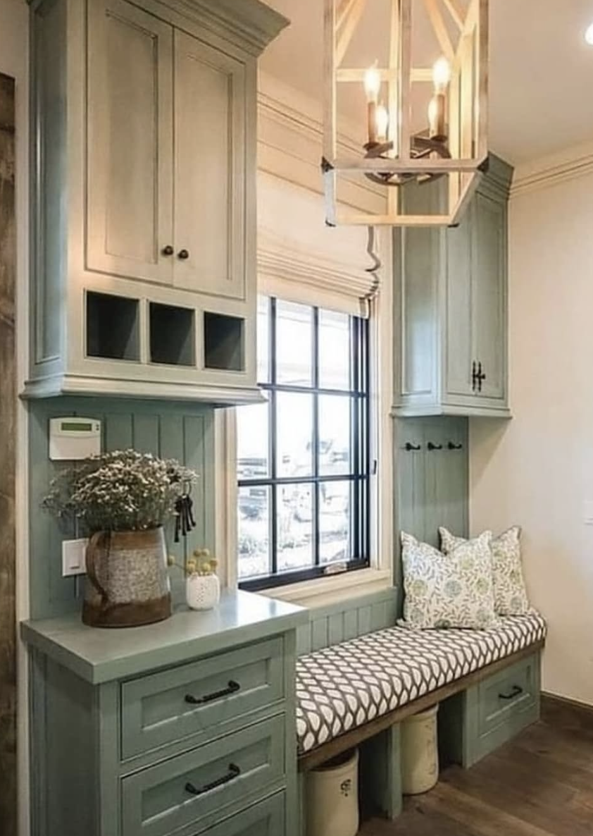 Built-in mudroom bench with patterned cushion, sage cabinetry, upper and lower storage, and window with black trim.