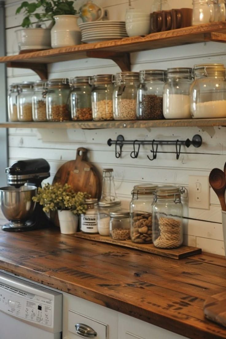 A cozy grandmacore kitchen with wooden shelves lined with mason jars filled with pantry staples, stacked dishware, and a rustic countertop decorated with flowers and vintage kitchen tools.
