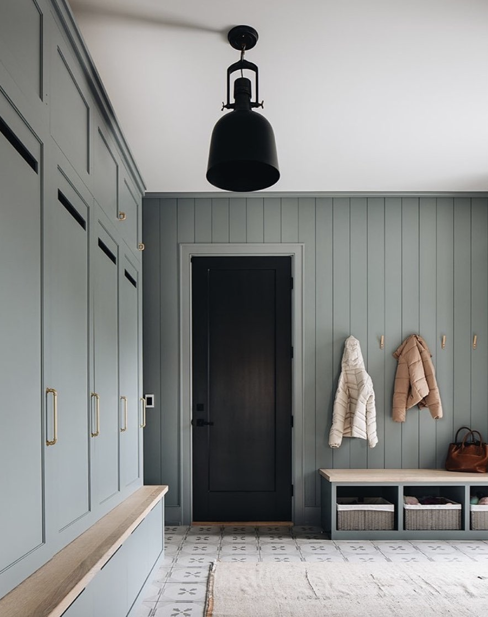 Mudroom with muted green built-in cabinets, wood bench seating, black interior door, and large modern pendant light.