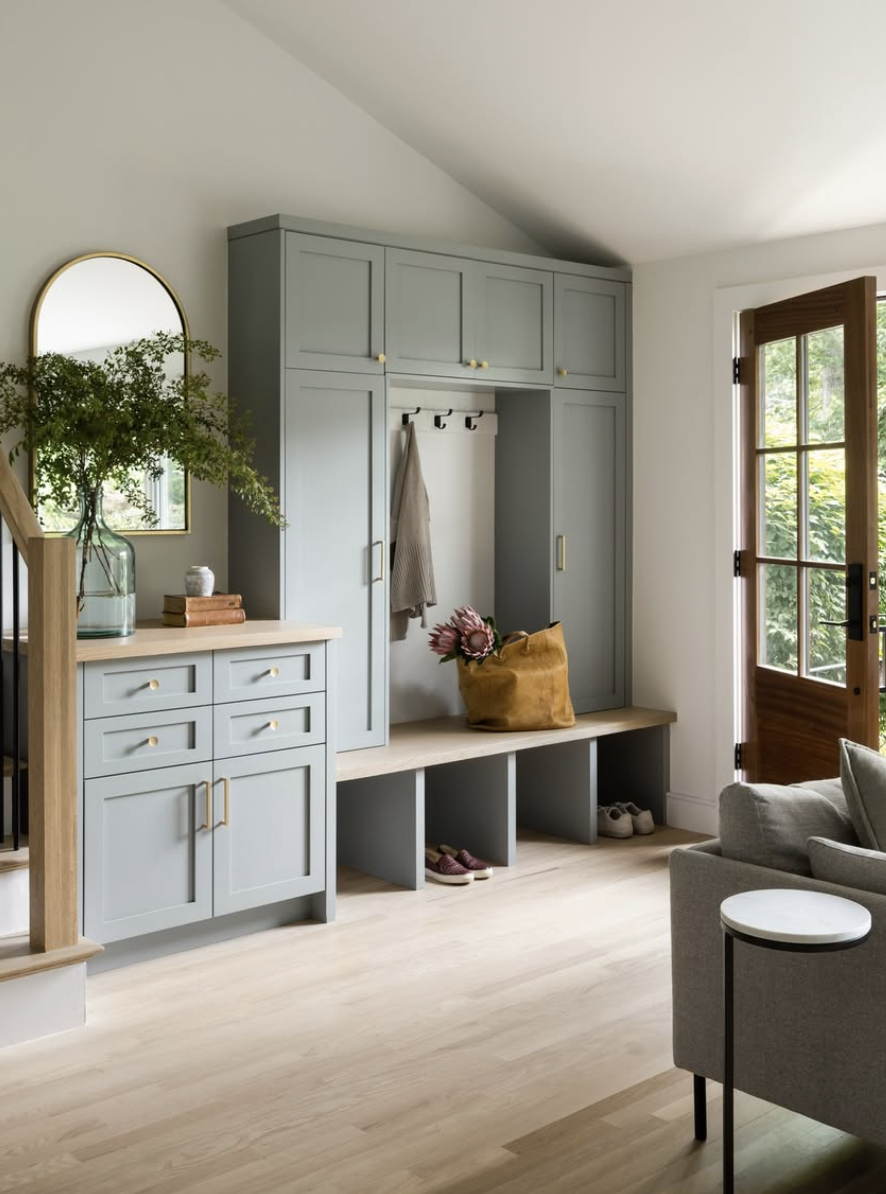 Mudroom with sage green built-in cabinets, wood bench seating, and open cubbies for shoe storage.