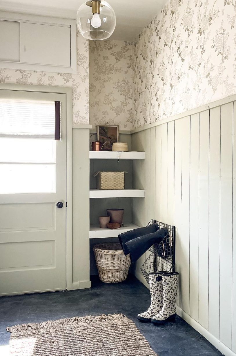 Sage green mudroom with half-wall paneling, floral wallpaper, built-in corner shelves, and boot storage.