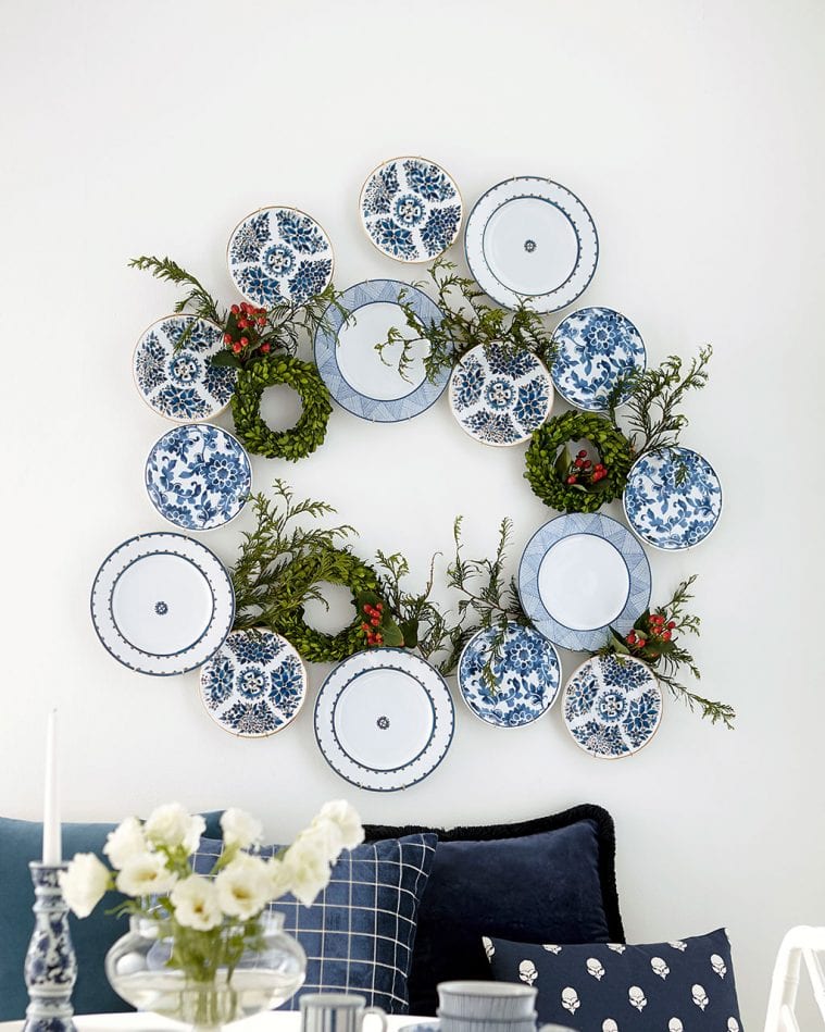 Christmas plate wall wreath made of blue and white patterned plates, greenery, and small red berries for a festive dining room accent.