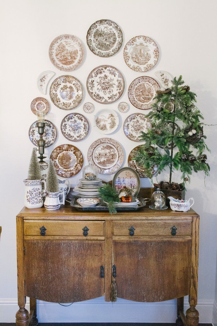 Christmas plate wall with brown transferware plates arranged in a circular pattern above a rustic wood sideboard decorated with bottle brush trees and a small Christmas tree.
