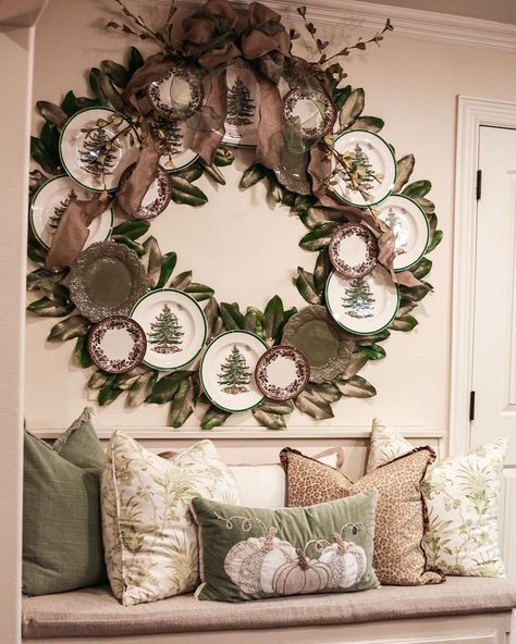Large Christmas wreath made of Spode Christmas Tree plates, green accents, and ribbon, displayed over a cozy bench with holiday pillows.