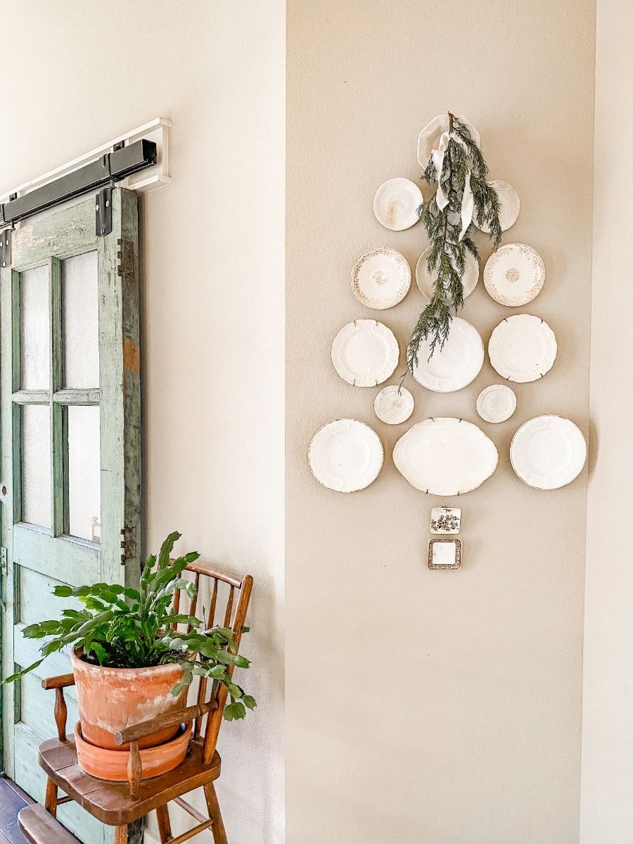 Neutral Christmas plate wall arranged in a tree shape with all-white plates and a simple greenery accent at the top.
