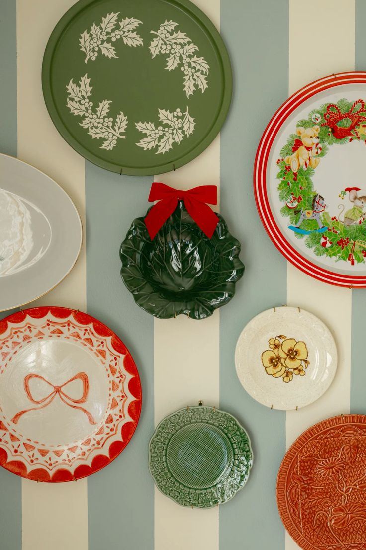 Christmas plate wall with colorful holiday plates, green holly wreath tray, red ribbon accent, and bold striped wall background.