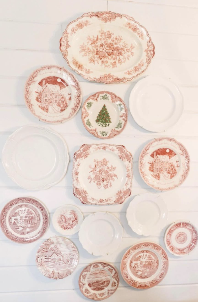 Christmas plate wall with red transferware and vintage holiday plates arranged in an eclectic gallery style on a white shiplap wall.