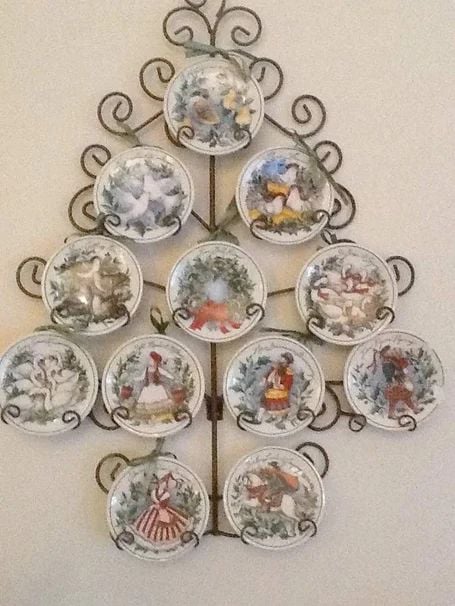 Christmas plate wall arranged in a tree shape with holiday-themed collector plates on a decorative metal frame.