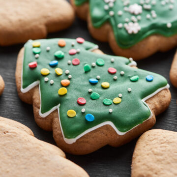 Close-up of a Christmas tree shaped sugar cookie decorated with green icing and festive sprinkles.