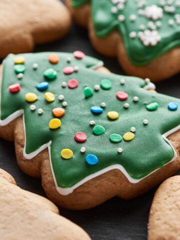 Close-up of a Christmas tree shaped sugar cookie decorated with green icing and festive sprinkles.