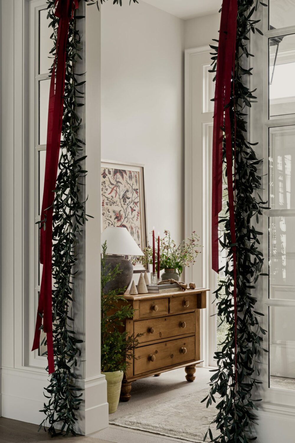 Studio McGee entryway decorated for Christmas with greenery garland and red ribbons, styled dresser with holiday candles and natural accents.