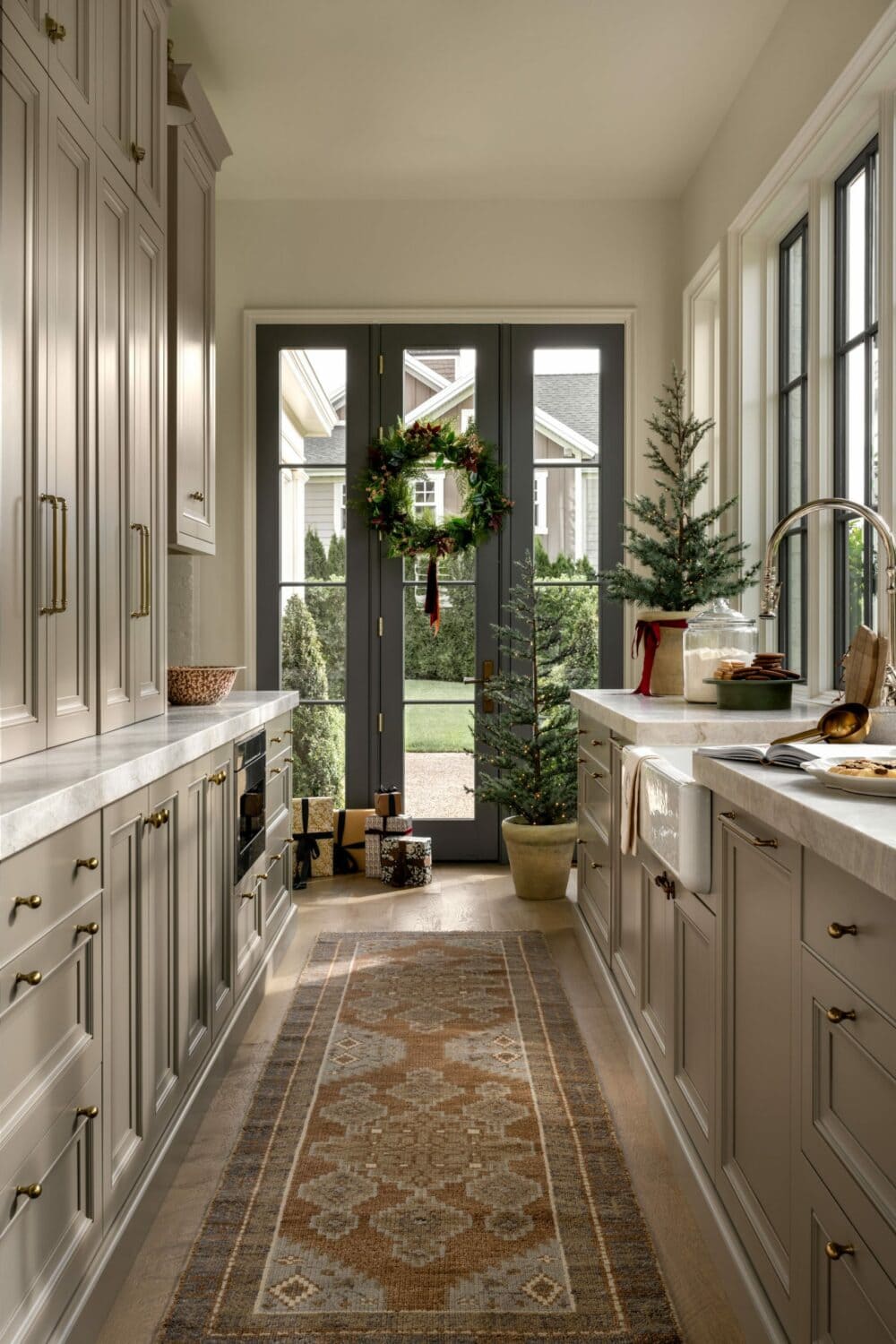 Studio McGee kitchen decorated for Christmas with a wreath on French doors, potted mini Christmas trees, and festive holiday accents.