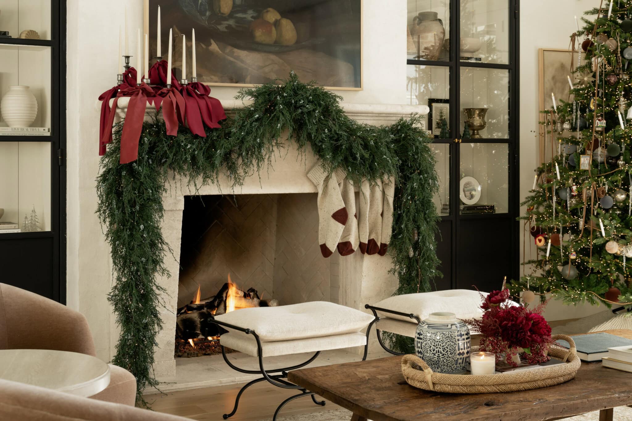Studio McGee Christmas mantel decorated with lush greenery, red ribbon candles, knit stockings, and Christmas tree with ornaments.
