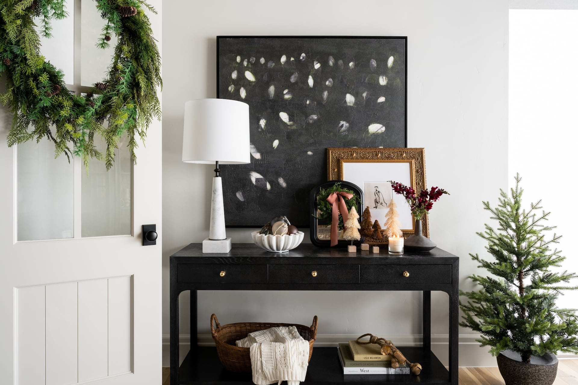 Studio McGee entryway styled for Christmas with black console table, mini holiday trees, greenery wreath, and modern holiday accents.