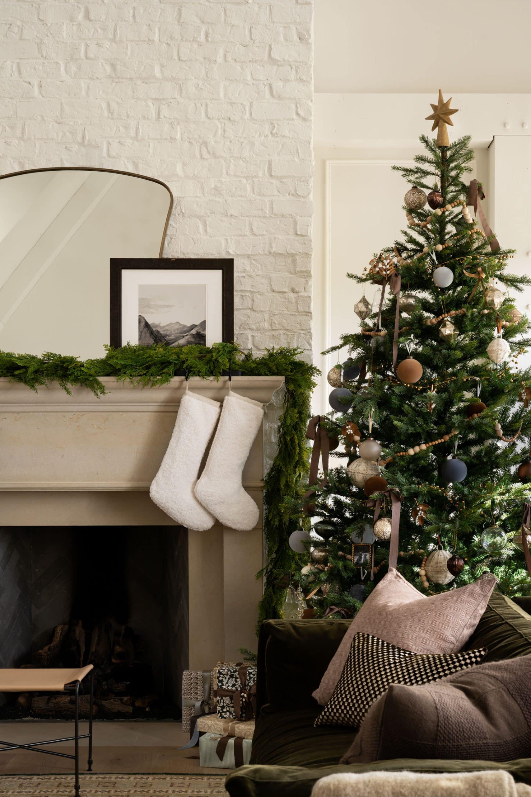 Studio McGee Christmas mantel with white stockings, greenery garland, and neutral decorated Christmas tree.