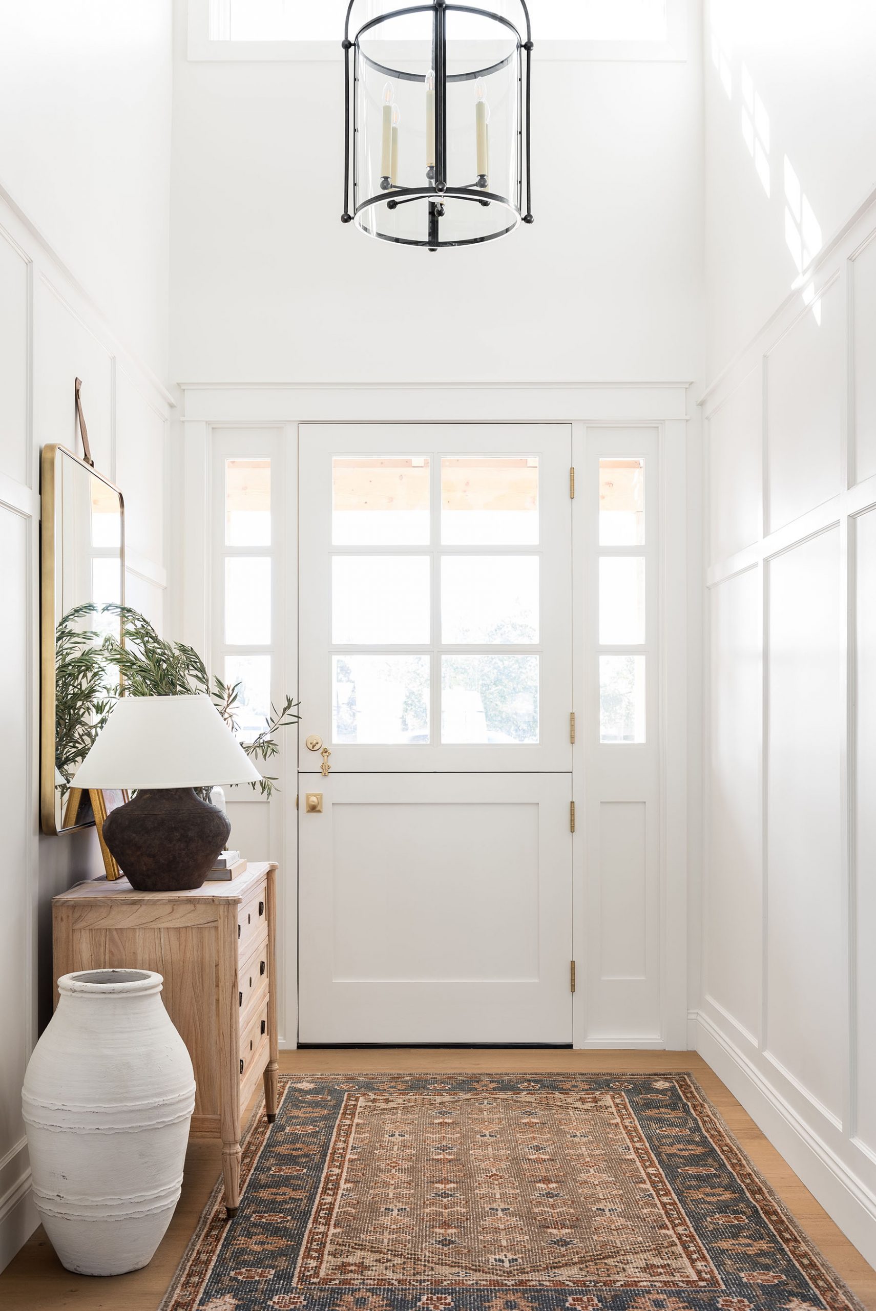 Bright neutral Studio McGee entryway with white walls, oak bench, vintage rug, and round mirror reflecting natural light.