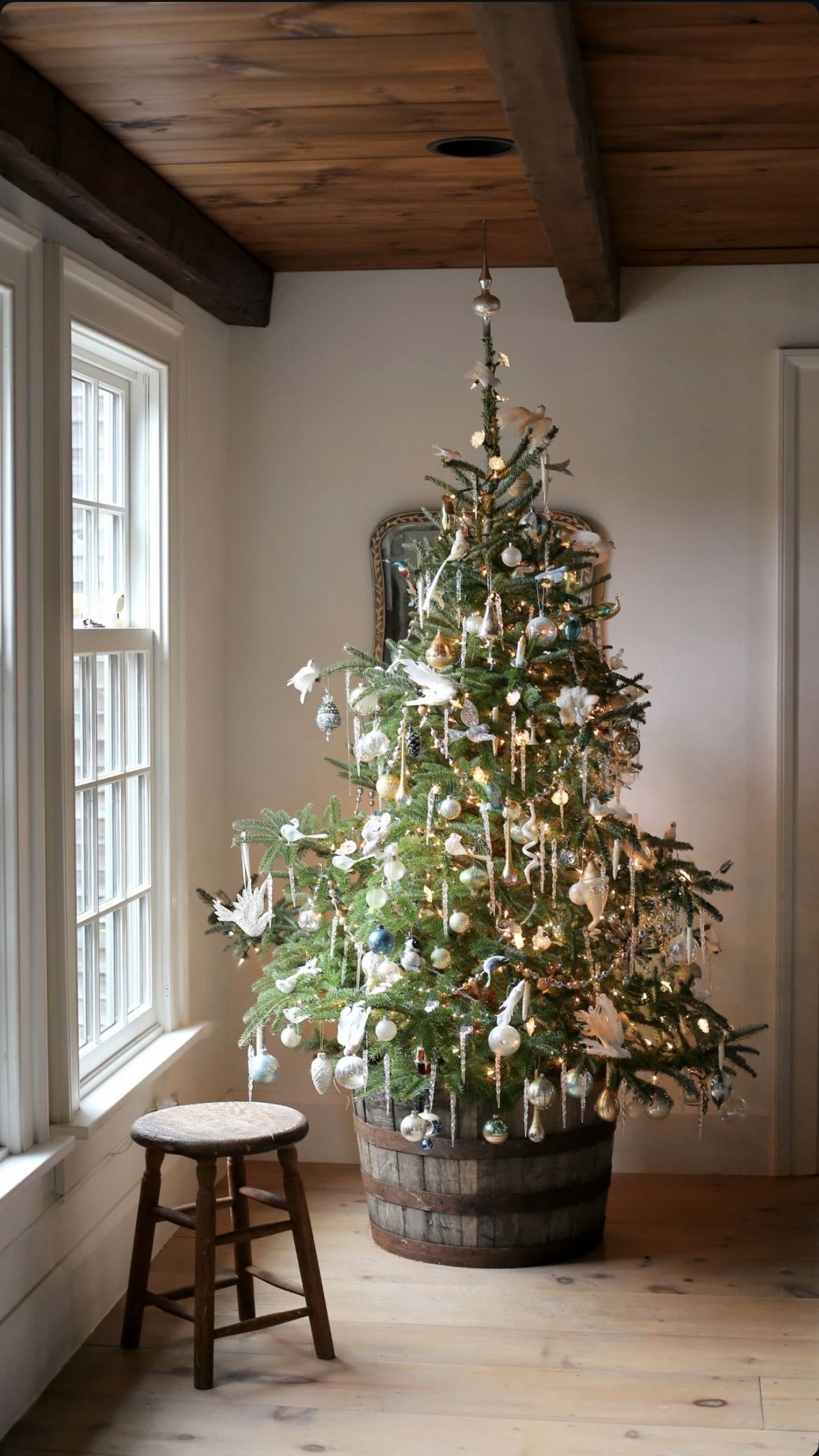Christmas tree with a rustic wooden barrel tree collar, white and gold ornaments, and warm lights for a vintage farmhouse holiday decor style.