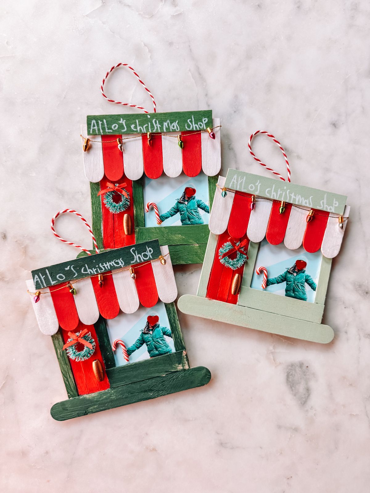 DIY popsicle stick storefront photo ornament painted in green, red, and white with a family photo and festive mini wreath accents