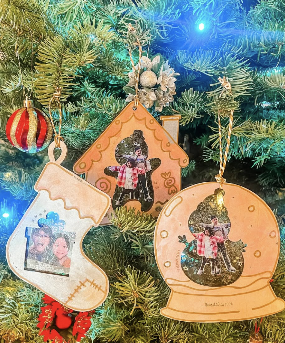 DIY photo ornaments and puzzles shaped like stockings, gingerbread houses, and snow globes with family pictures hanging on a Christmas tree