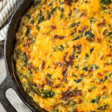 Creamy baked Spinach Maria Dip in a cast iron skillet topped with melted cheddar and mozzarella cheese, ready to serve with bread and chips.