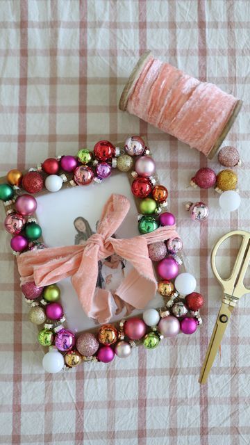 DIY colorful bauble frame photo ornament decorated with mini Christmas ornaments, a pink velvet ribbon bow, and a family photo on a plaid background