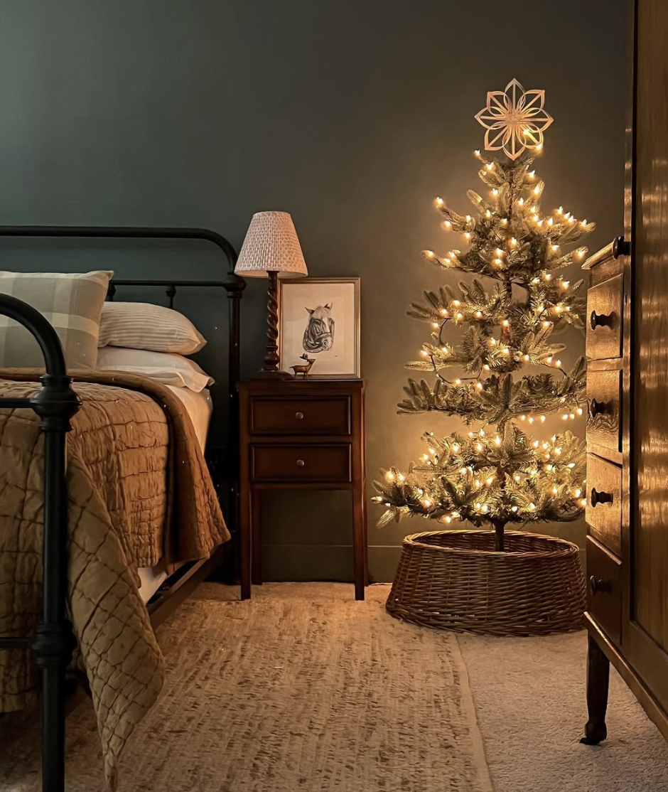 cozy farmhouse christmas bedroom with dark green walls, small lit christmas tree, and rustic wood furniture