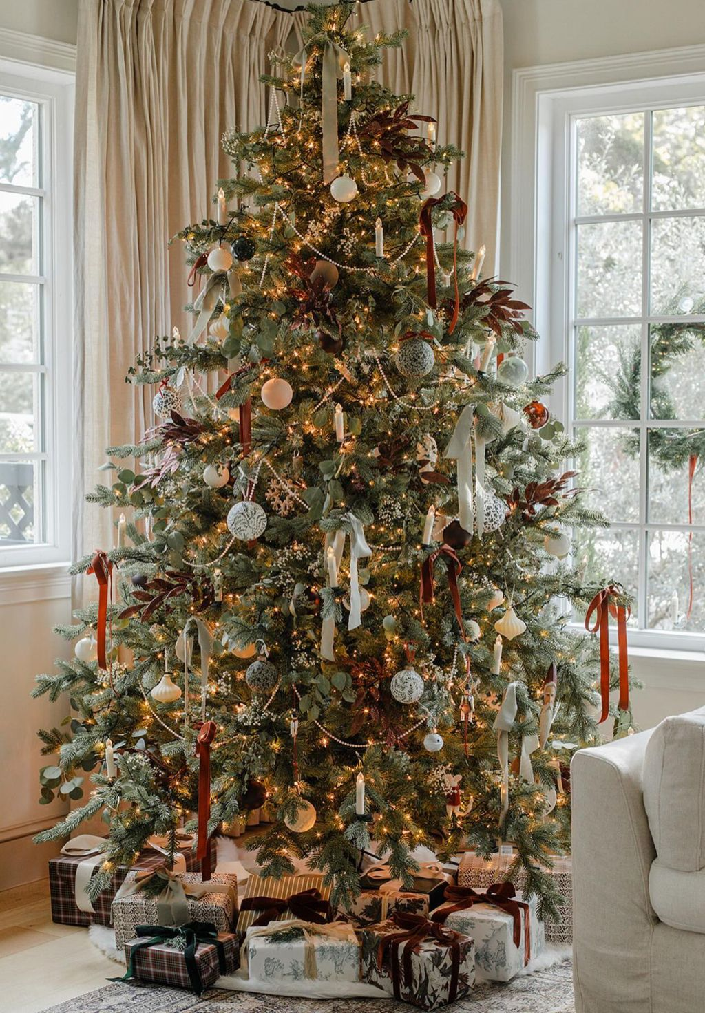elegant farmhouse Christmas tree decorated with velvet ribbons, eucalyptus sprigs, and neutral ornaments surrounded by wrapped gifts in a cozy living room