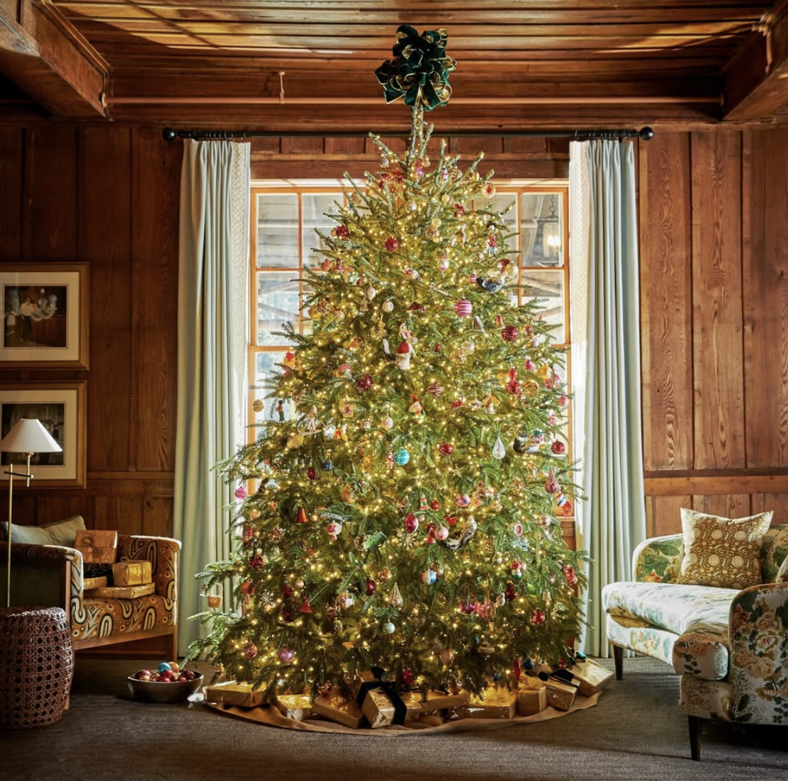 cozy farmhouse Christmas tree with colorful vintage ornaments and twinkle lights in rustic wood-paneled living room