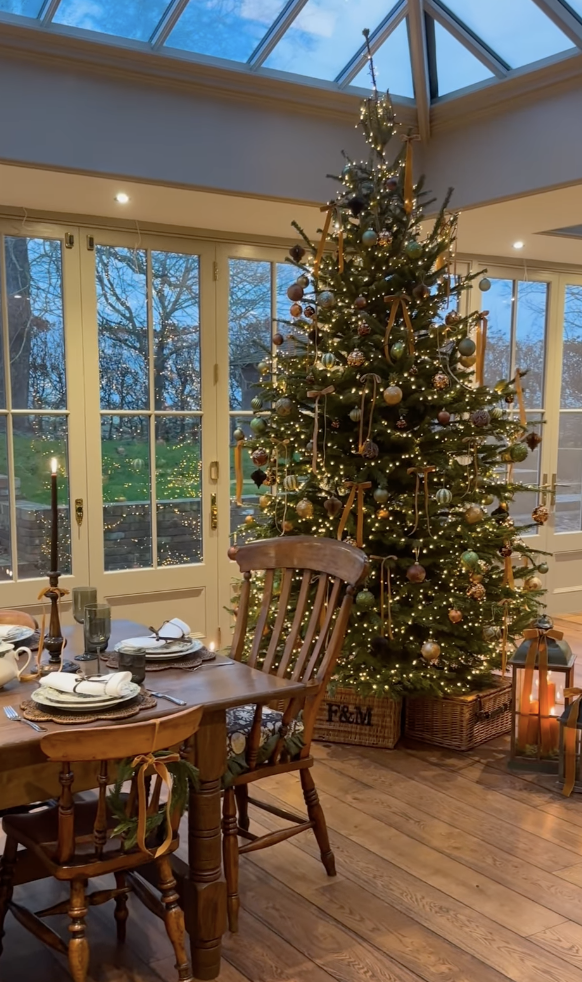 cozy farmhouse Christmas tree with gold ribbon and vintage ornaments in rustic dining room with wood floors and candle lanterns