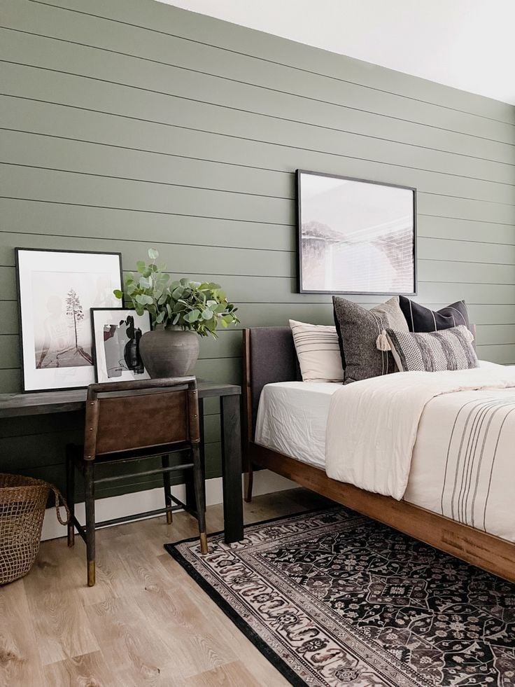 Modern bedroom with dark green horizontal shiplap accent wall, wood bed frame, neutral bedding, and black framed artwork.