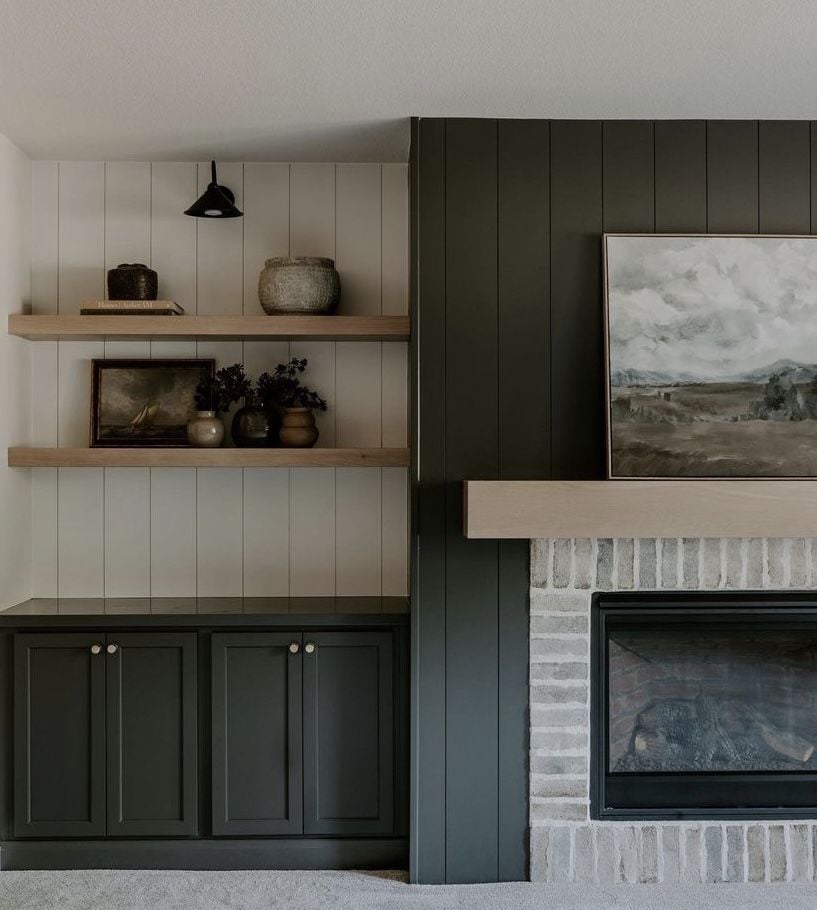 Fireplace wall with dark green vertical shiplap surround, brick fireplace, light wood mantel, and built-ins with floating shelves.