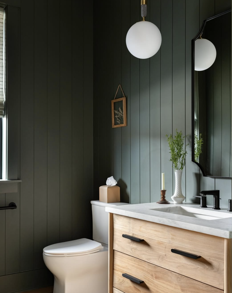 Bathroom with dark green vertical shiplap walls, globe pendant light, wood vanity with black hardware, and modern black mirror.