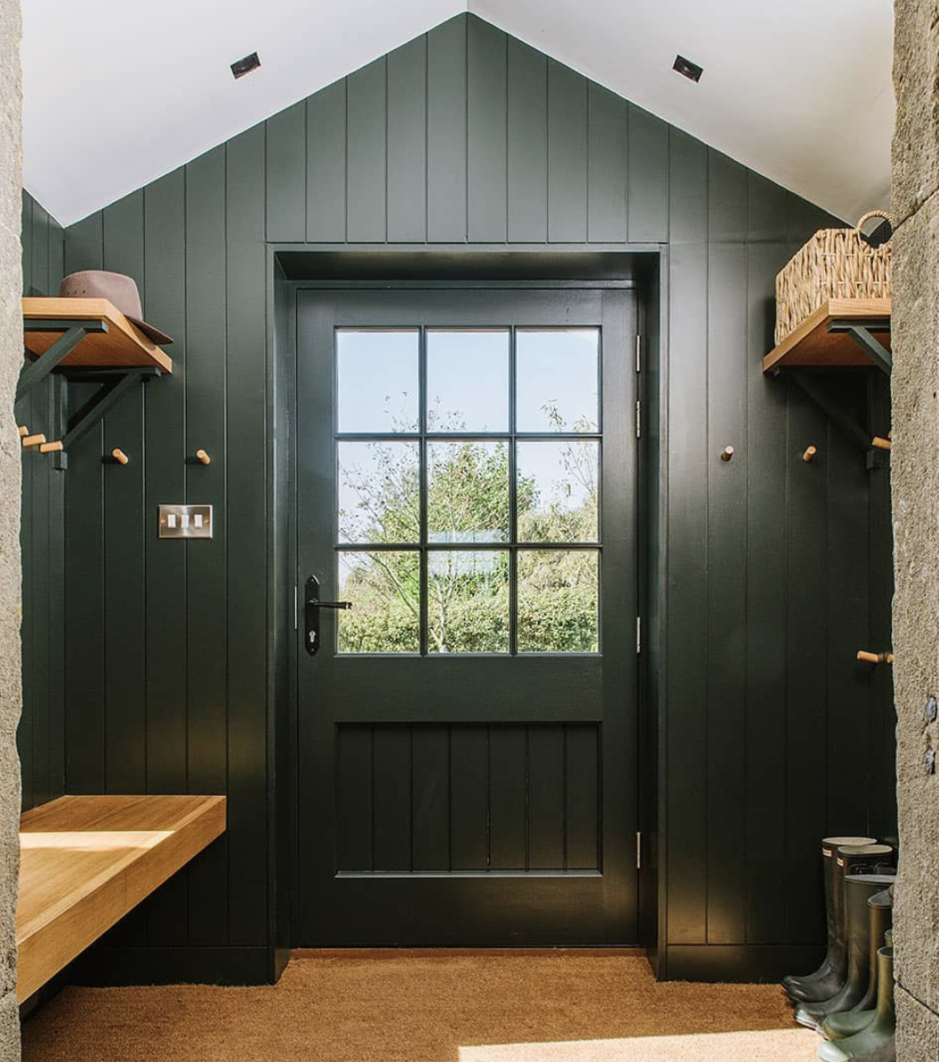 Dark green vertical shiplap entryway with matching door, wood bench, peg hooks, and vaulted white ceiling.