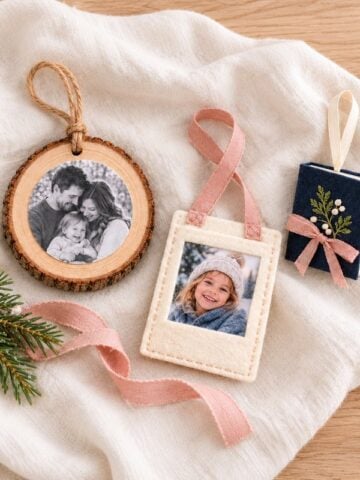 Wood slice photo ornament, cream felt photo pocket, and closed navy photo book arranged on ivory linen with blush ribbon and greenery.