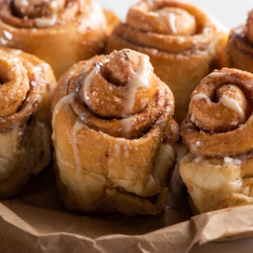 Freshly baked cinnamon buns drizzled with creamy icing, showing soft golden layers and gooey cinnamon filling.
