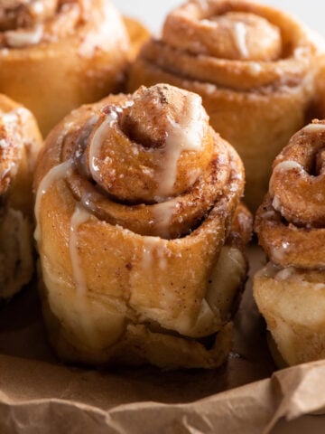 Freshly baked cinnamon buns drizzled with creamy icing, showing soft golden layers and gooey cinnamon filling.
