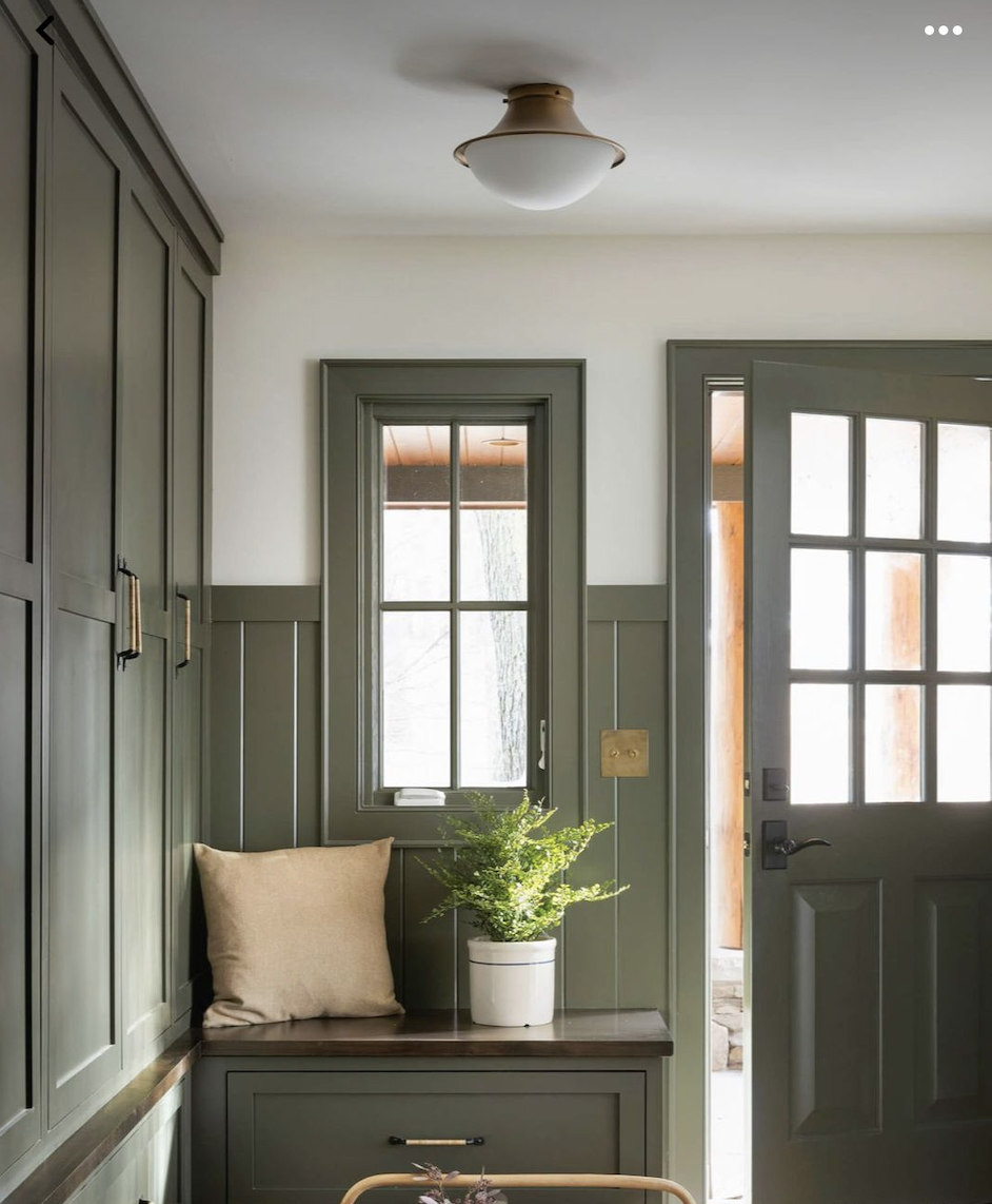 Mudroom with green shiplap wainscoting, built-in bench seating, storage cabinets, hex tile floor, and a green door with window panes.