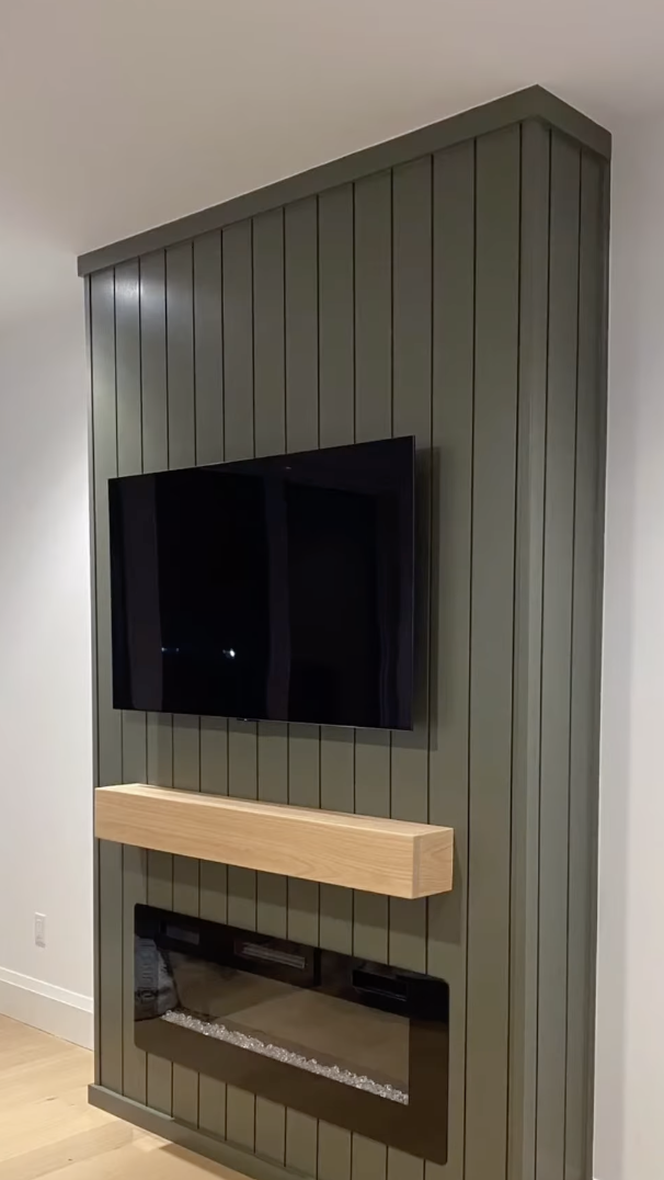 Living room with green vertical shiplap fireplace wall, floating light wood mantel, and mounted TV above black electric fireplace insert.
