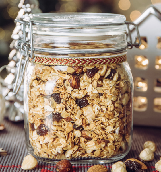 Homemade granola in a mason jar with nuts and raisins, decorated with holiday ribbon and Christmas decor in the background.