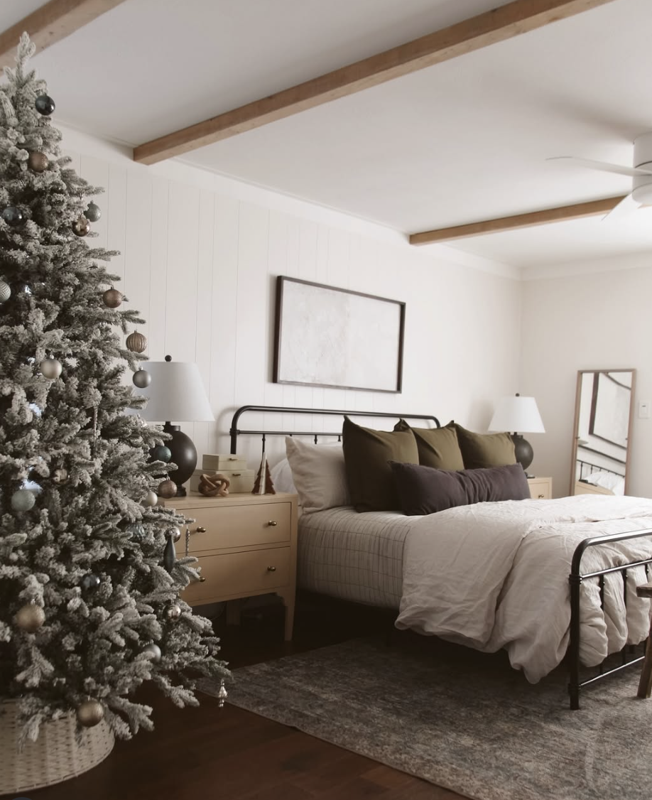 modern farmhouse christmas bedroom with flocked christmas tree, neutral bedding, and wooden ceiling beams