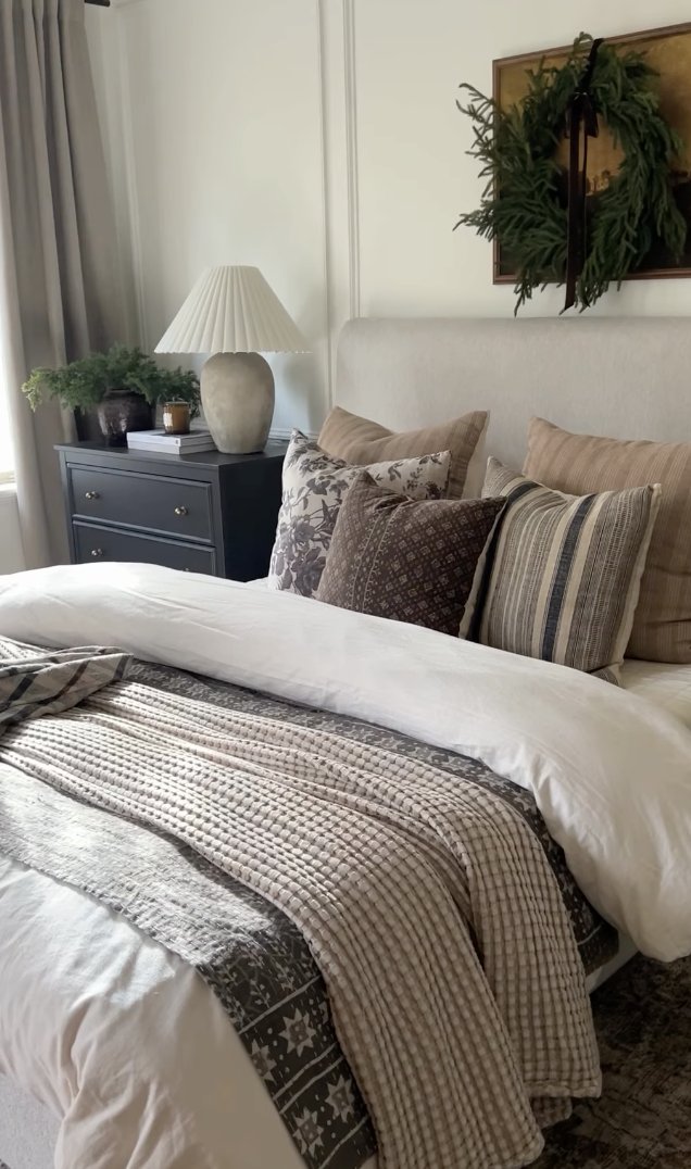 modern farmhouse christmas bedroom with neutral pillows, black dresser, and greenery wreath above headboard